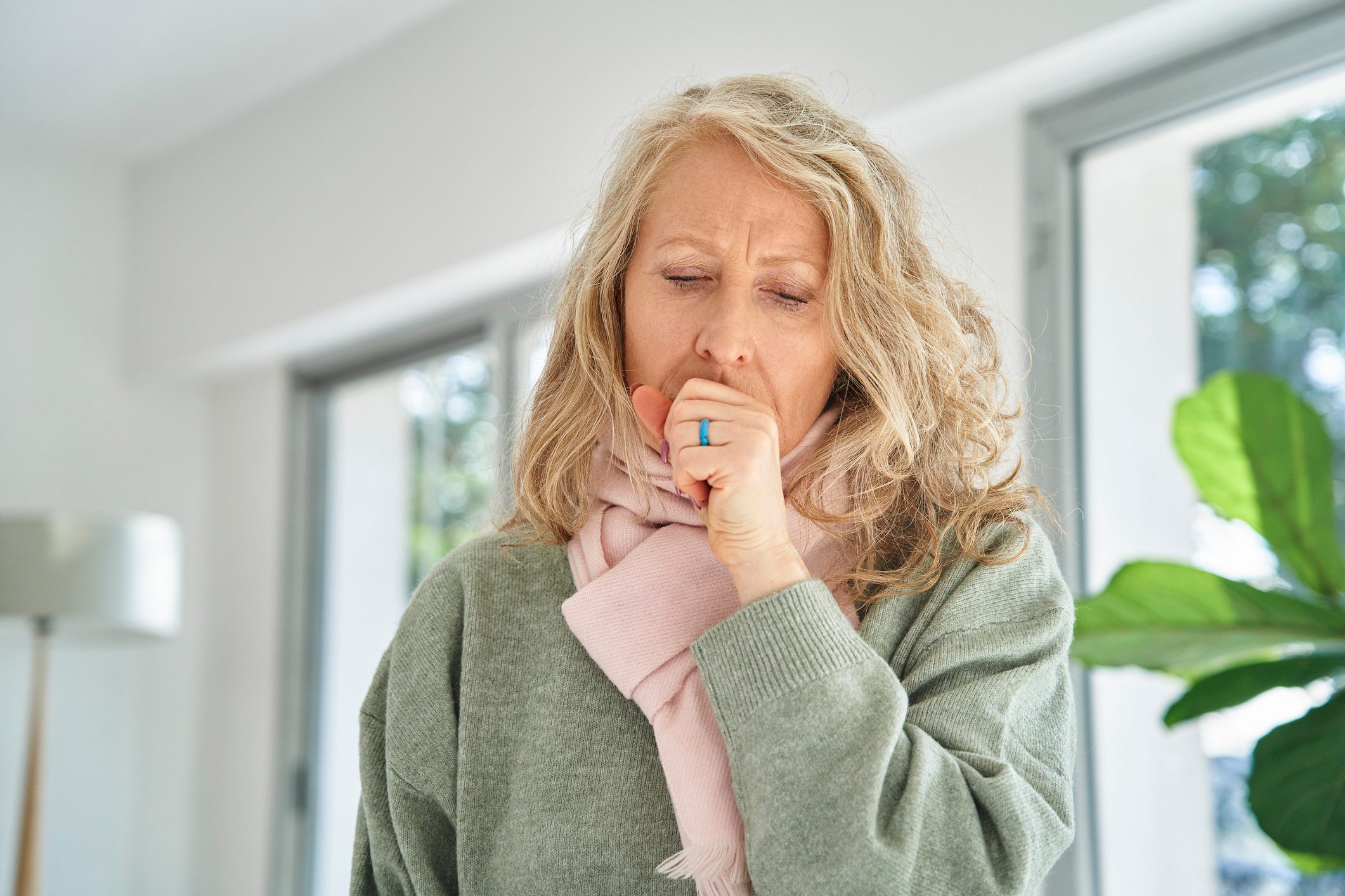 Senior woman sitting indoors while coughing