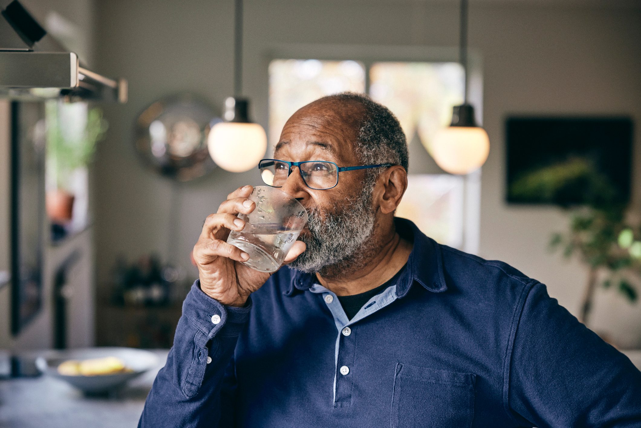 Contemplative senior man drinking water at home