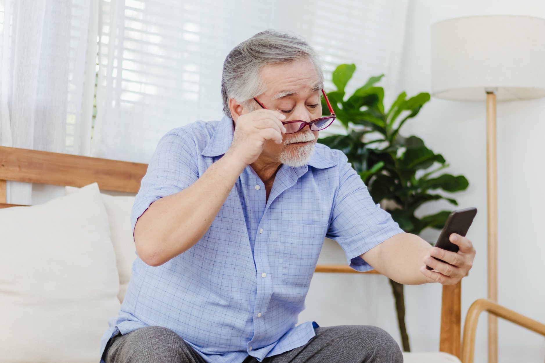 Asian senior fatigue man taking off glasses during using smartphone