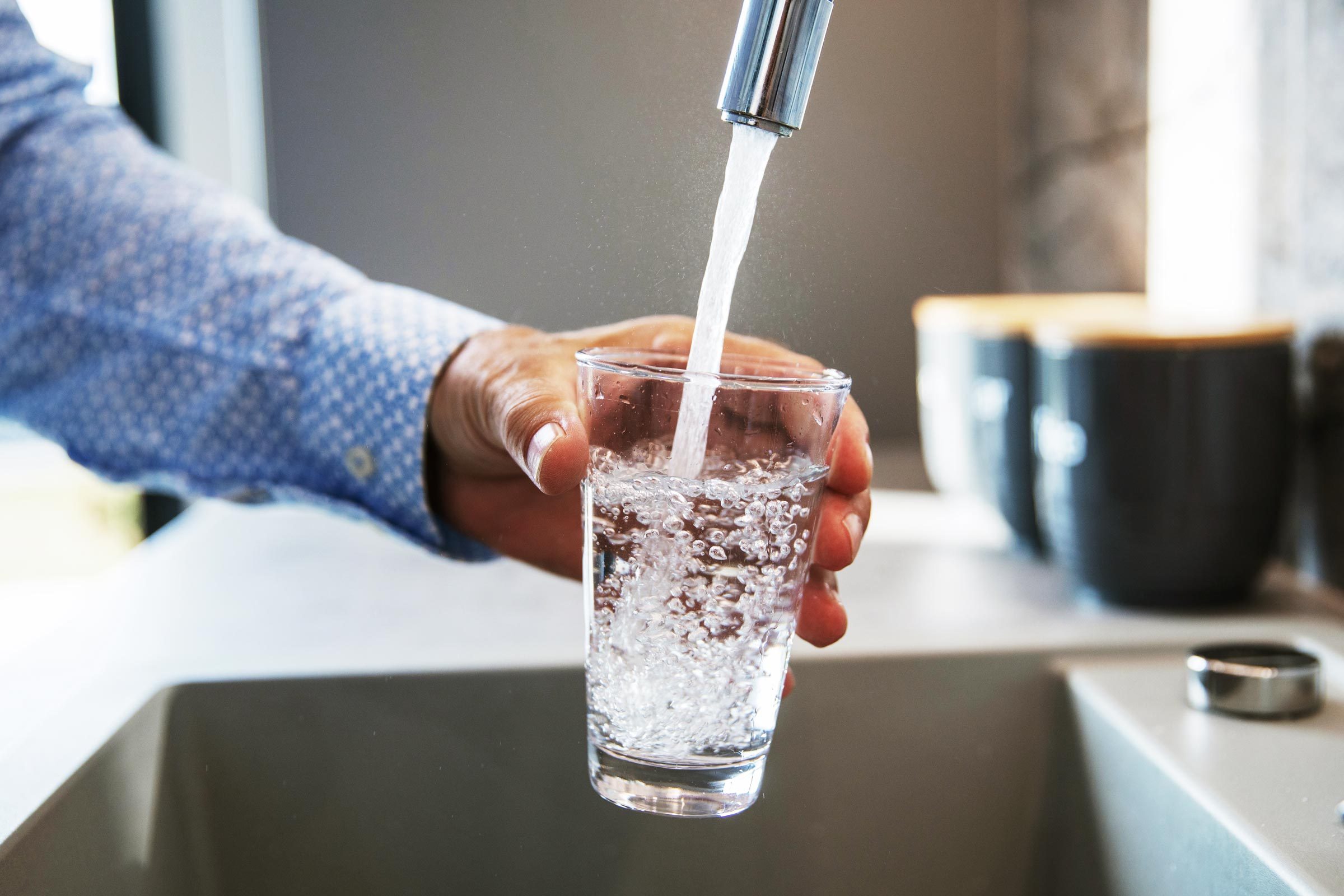 man filling a glass of water from his kitchen sink tap