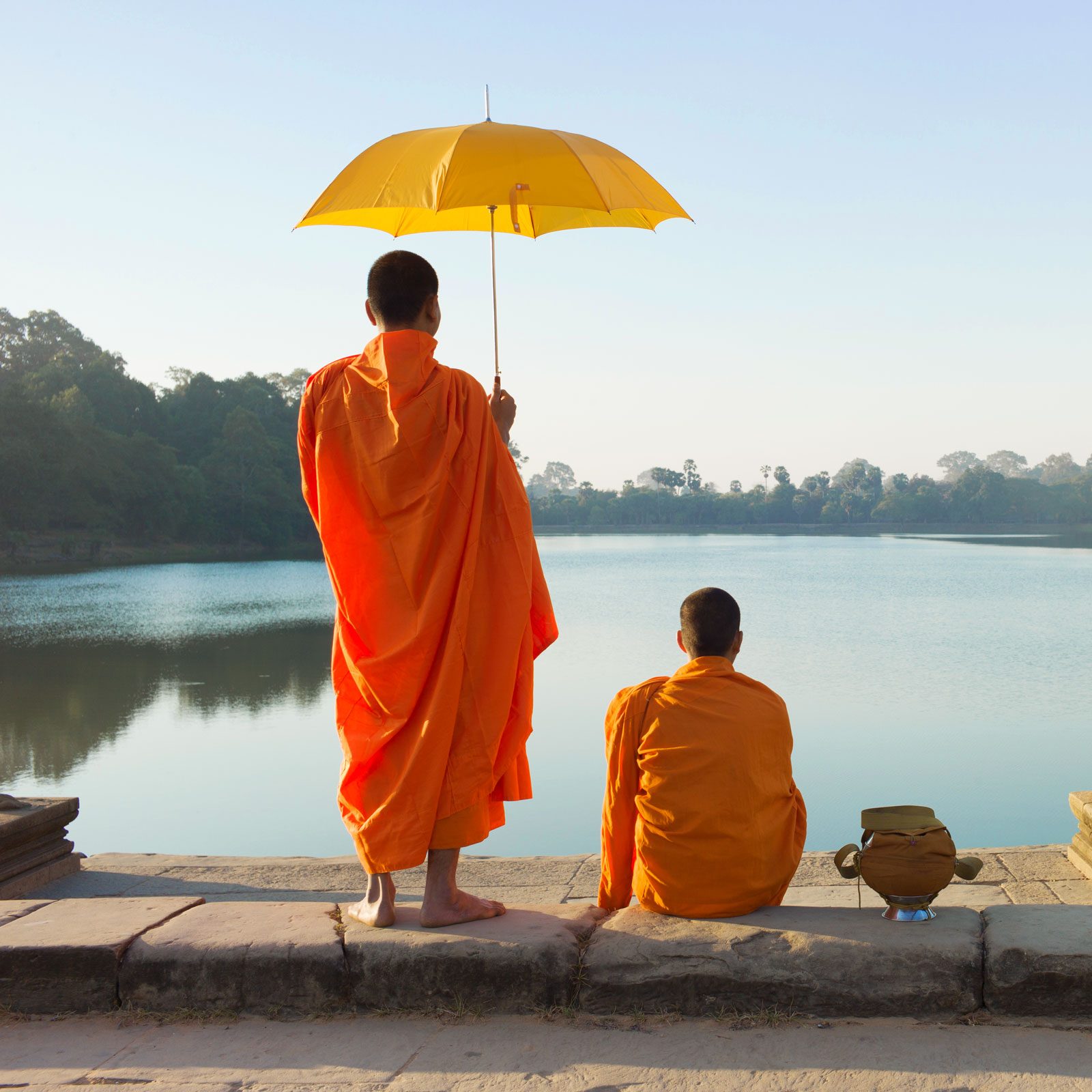 two monks looking at the water, one holding a yellow umbrella