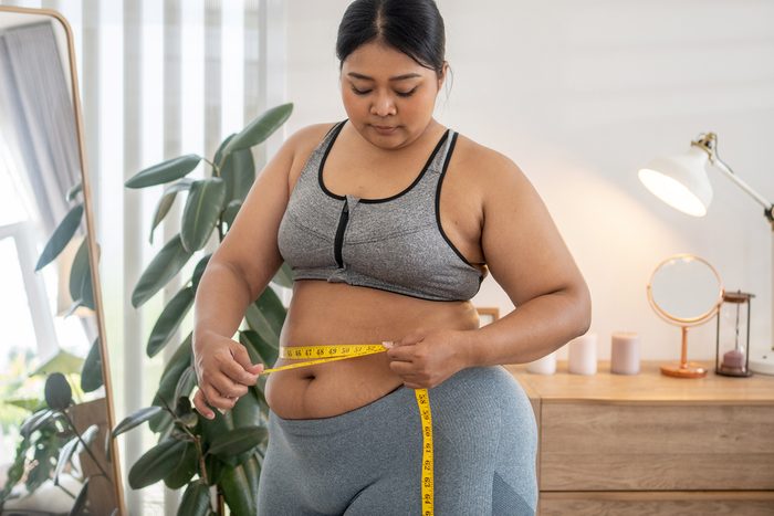 plus size female holds measures tape check her waist size