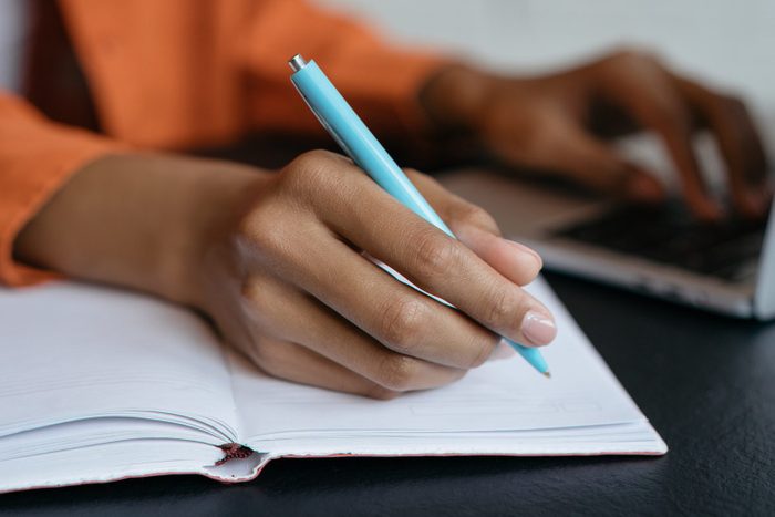 Close-up shot of student hand holding pen and writing in notebook, working at home. E-learning