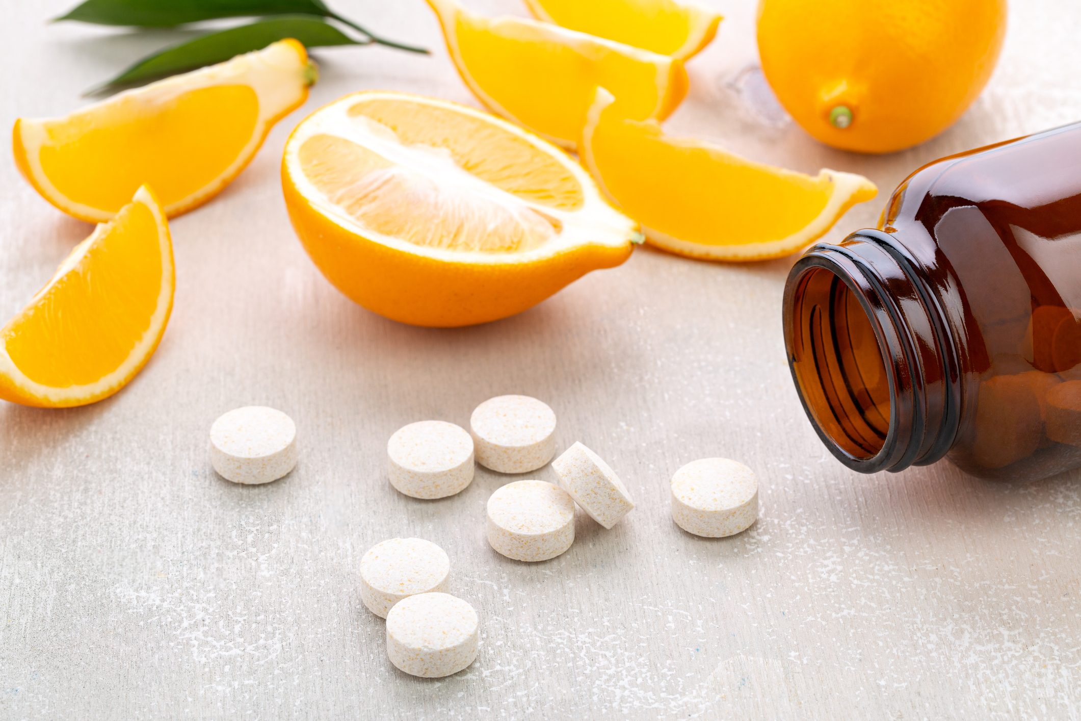 Vitamins lying near dark glass jar with lemon slice and whole fruit on white wooden table