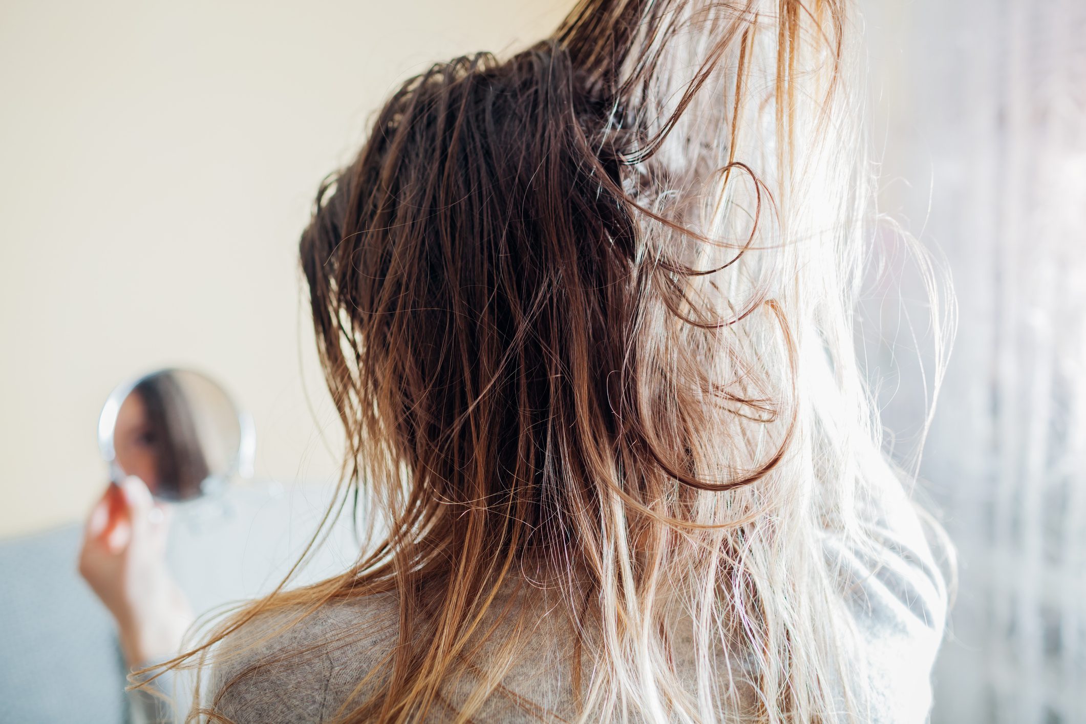 Close up of woman touching dirty oily and greasy hair looking in mirror at home. Time to wash head with shampoo