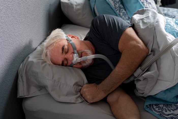 A 60-year-old man sleeps with a CPAP machine in bed to treat his sleep apnea, a condition where breathing repeatedly stops and starts during sleep.