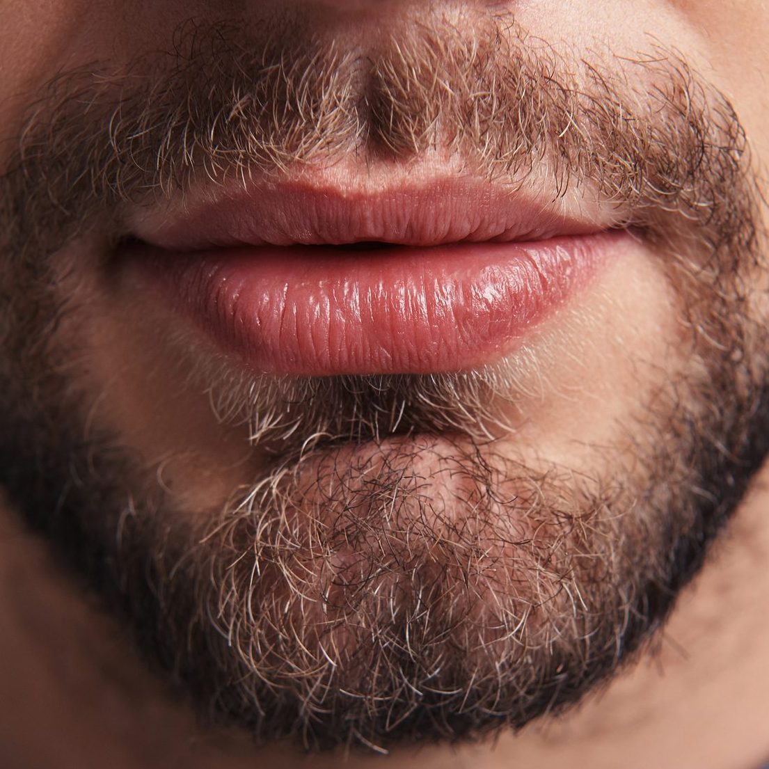 Close up of young unshaved man standing against grey background