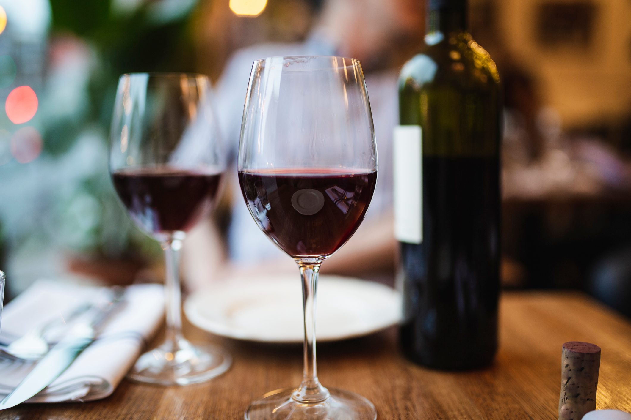 a restaurant table with two glasses of red wine poured from the bottle nearby