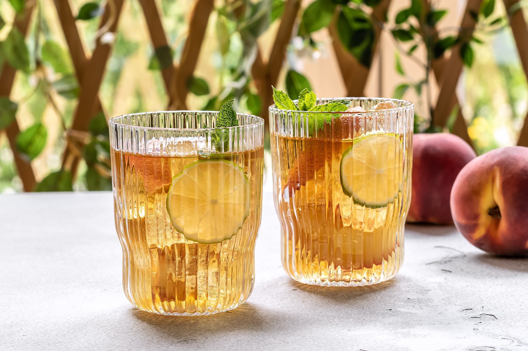 Two glasses of hard kombucha on a table with peaches nearby