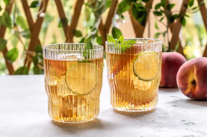 Two glasses of hard kombucha on a table with peaches nearby