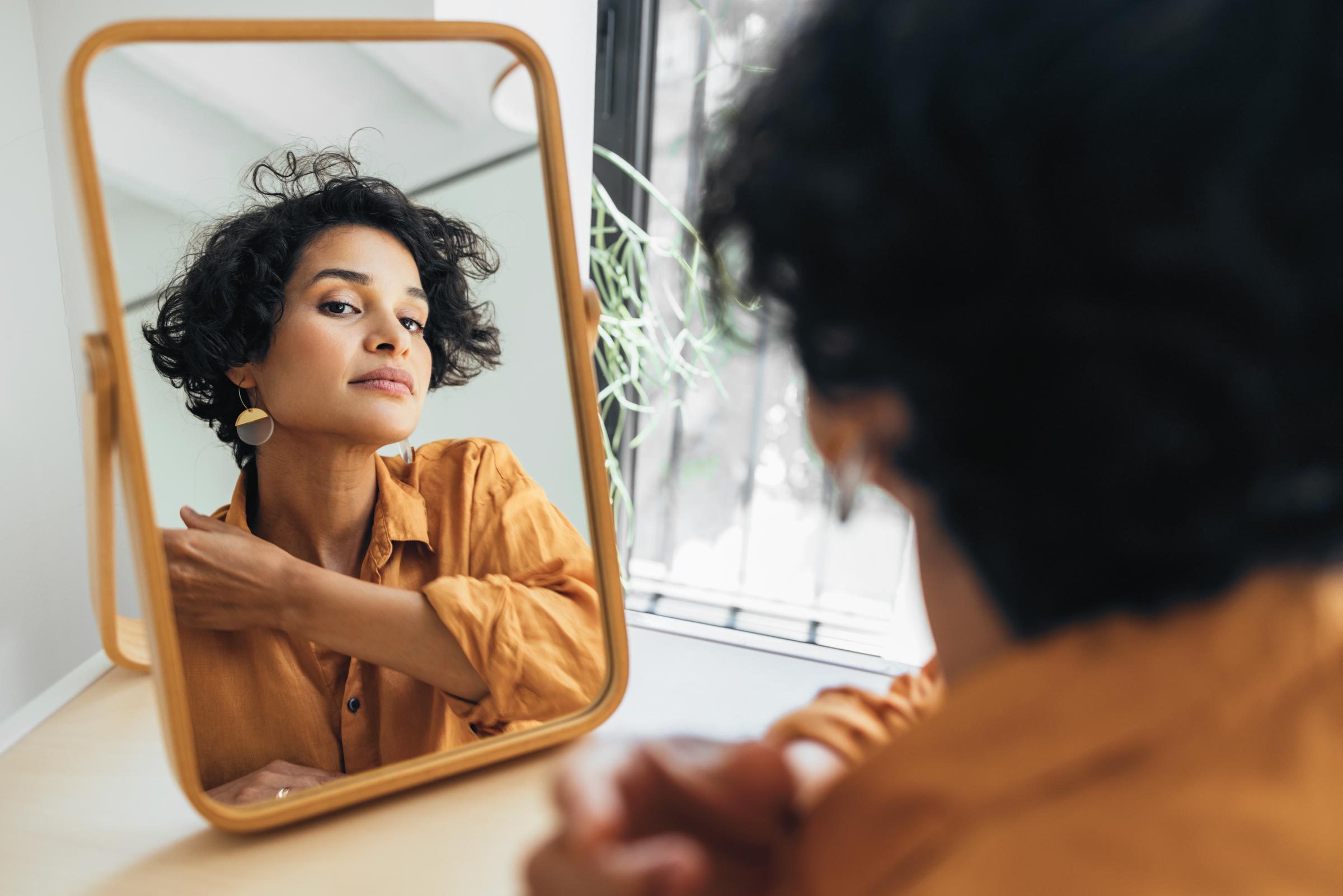 A Beautiful Natural Woman Looking At Her Face In The Mirror And Checking Her Make Up