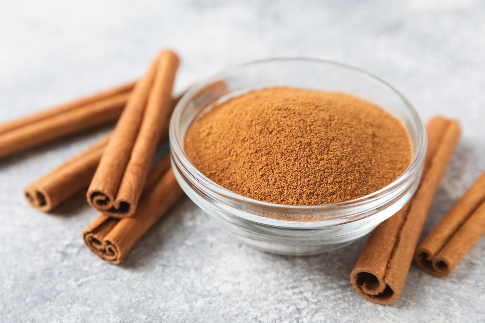 Cinnamon powder in a bowl on a textured wooden background. Spicy spice for baking, desserts and drinks. Fragrant ground cinnamon. Cinnamon stick. Place for text. Copy space.