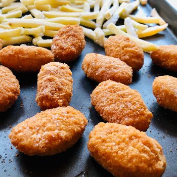 Frozen chicken nuggets and French fries on baking pan