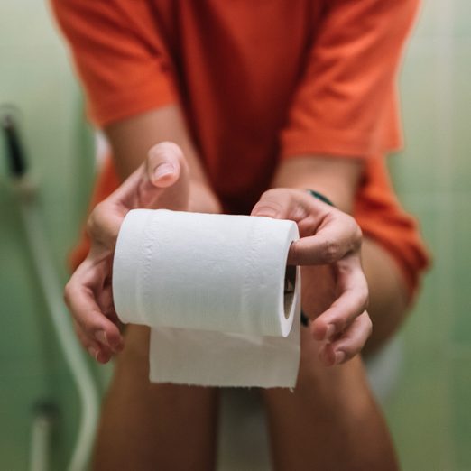 Woman Sitting On Toilet Holding Toilet Paper Roll