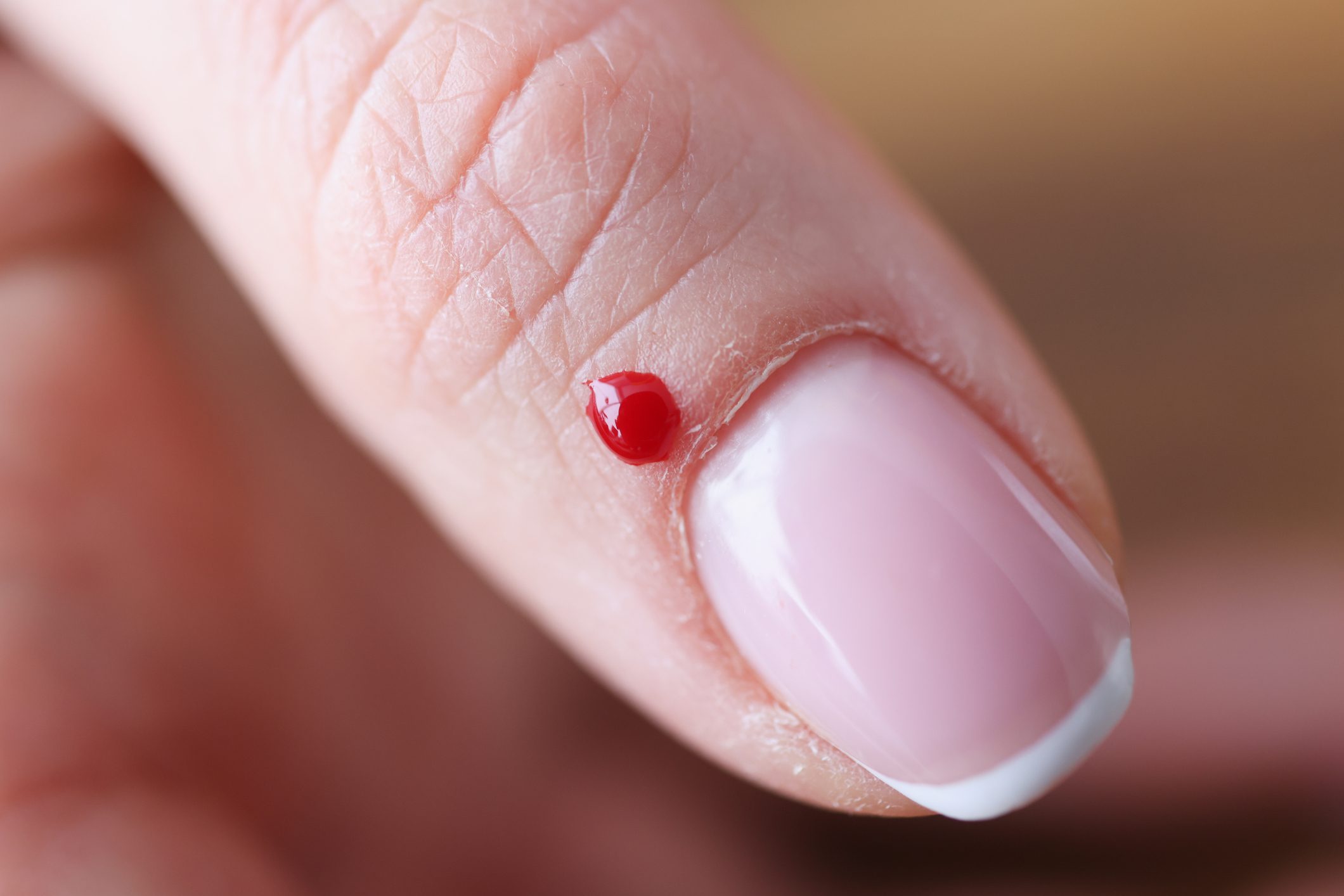 Closeup of drop of blood near womans nail