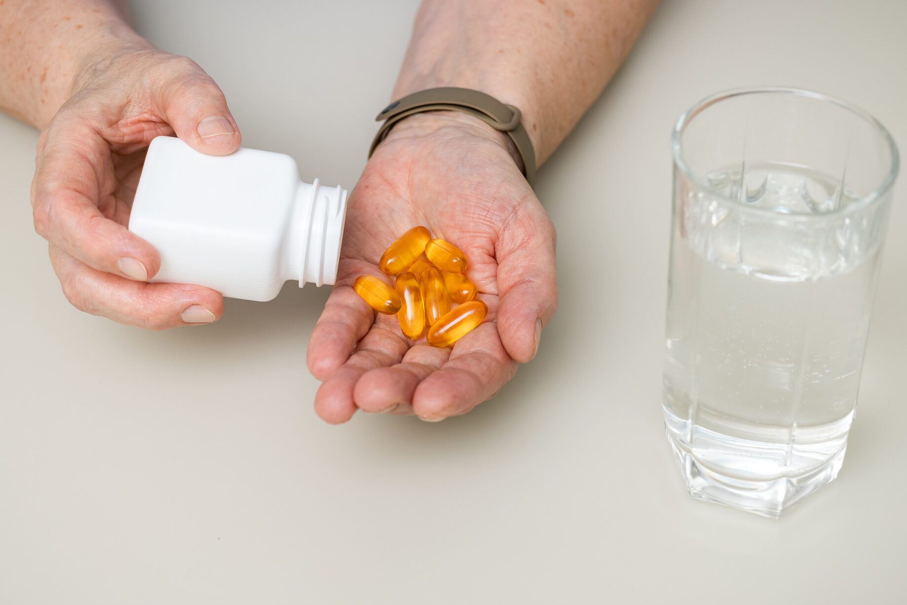 Senior woman with wrinkled old hands at the table pouring from a bottle omega 3 yellow capsules into palm. Healthcare and medicine concept