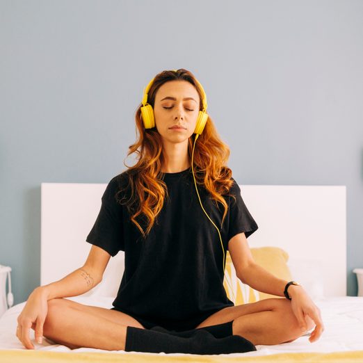 Young Woman Meditating On Bed At Home With Headphones