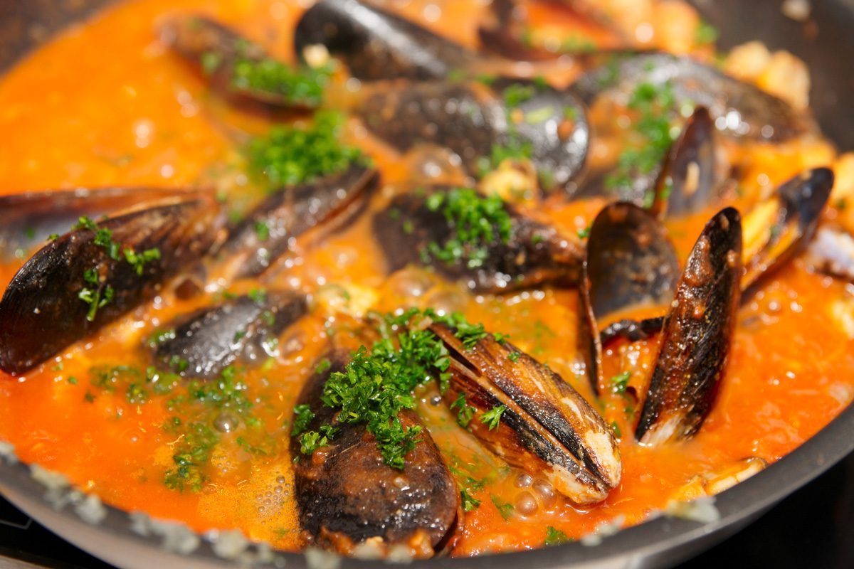 Mussels being fried in pan with tomato sauce