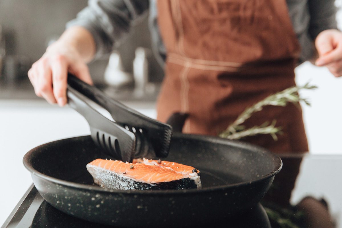 lady standing in kitchen while cooking fish