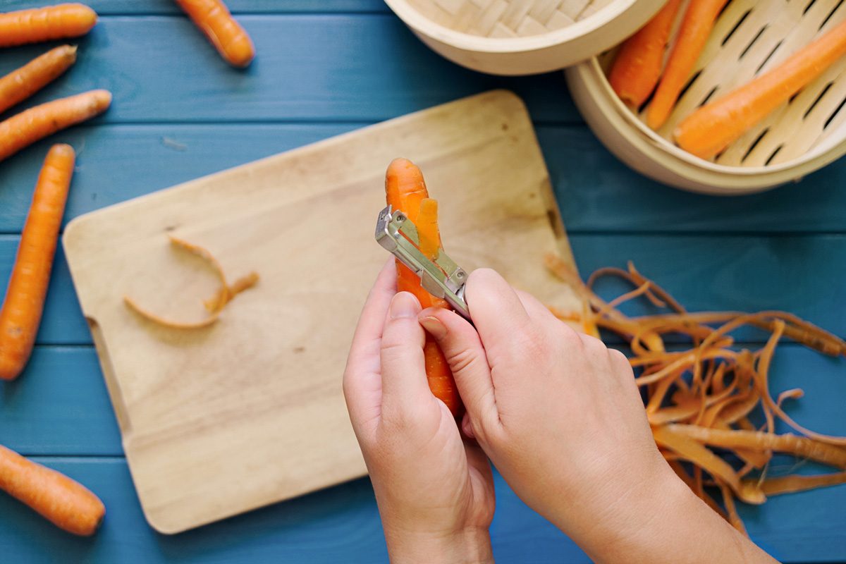 hands peeling an orange carrot on blue background