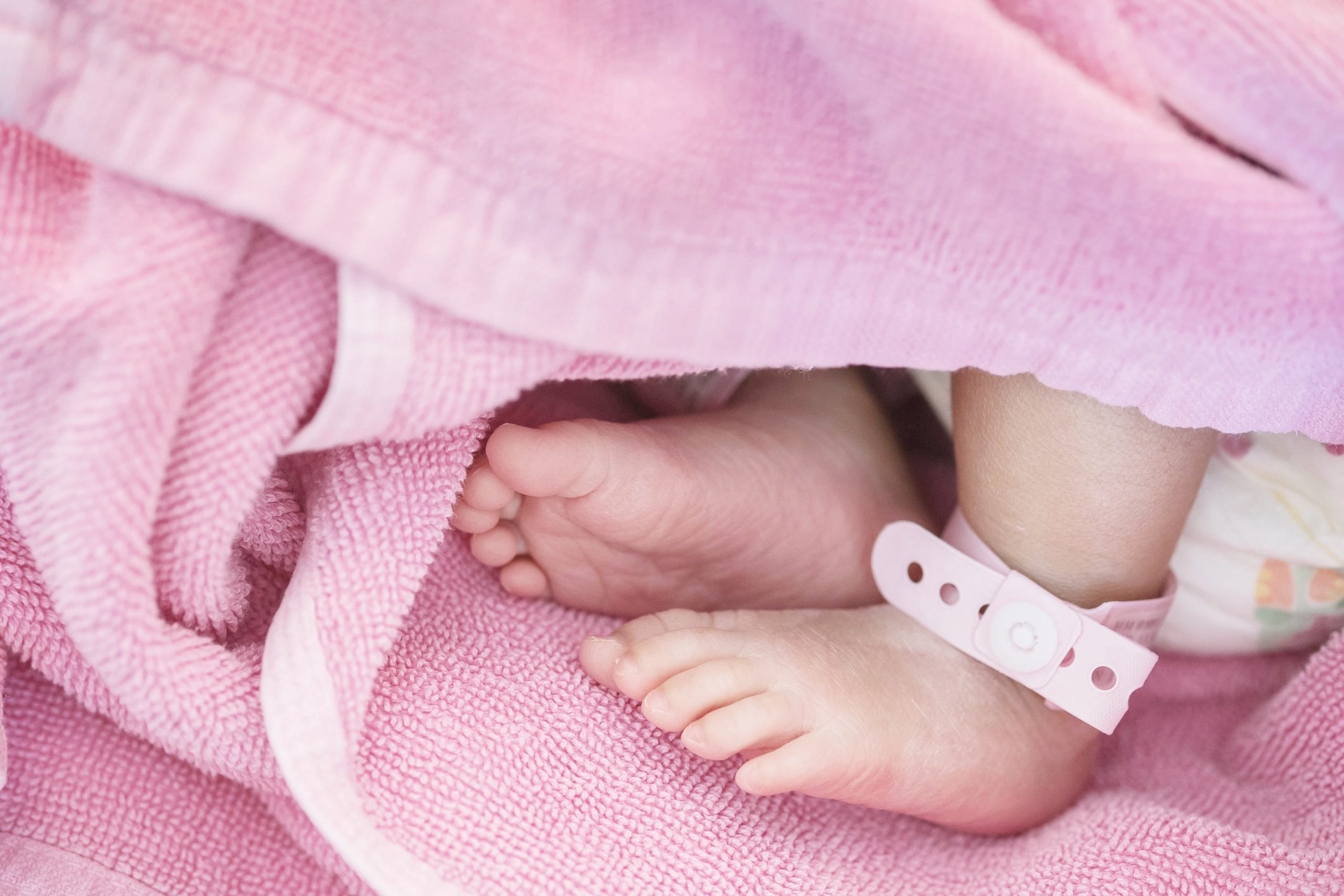 Closeup Foot Of Baby With Newborn Ankle Tag On Bed In Hospital Textured Background